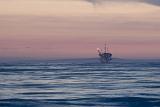 Offshore oil rig in the Gulf of Mexico off California at dusk with a colorful pink sky above a calm ocean