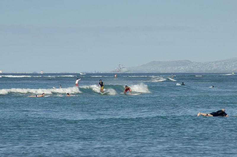Few Tourists Surfing at Blue Water Waikiki Beach. Isolated Light Blue Gray Sky Background.