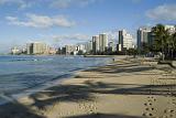 Scenic view of the waterfront and city skyline with footsteps across the golden sand of Waikiki beach, Honolulu, Hawaii