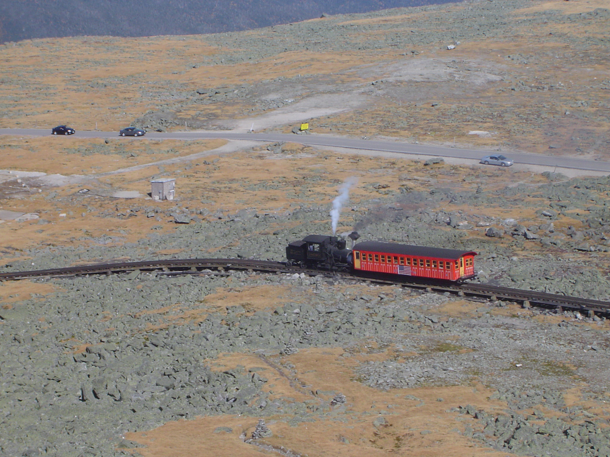 an image of Mount Washington Cog Railway traversing a steep slope with a single carriage carrying tourists on a sightseeing tour