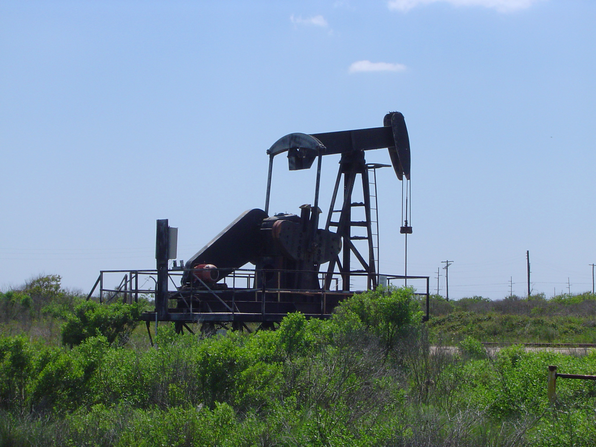 an image of Iconic Nodding Donkey - Oil Well Pump Jack on Grassy Land. Captured on Light Blue Sky Background.