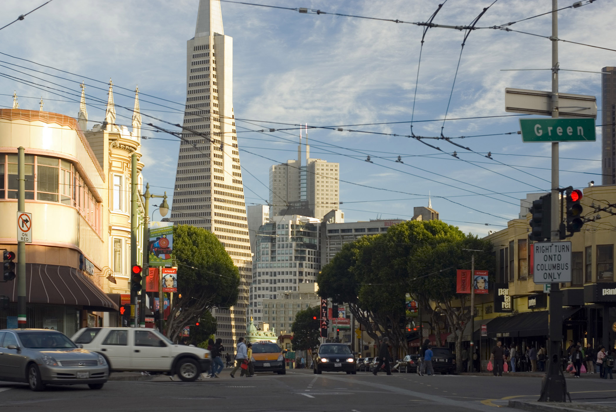 an image of Street level scene of a busy intersection with traffic and pedestrians on Columbus Avenue San Francisco with the Transamerica Pyramid behind