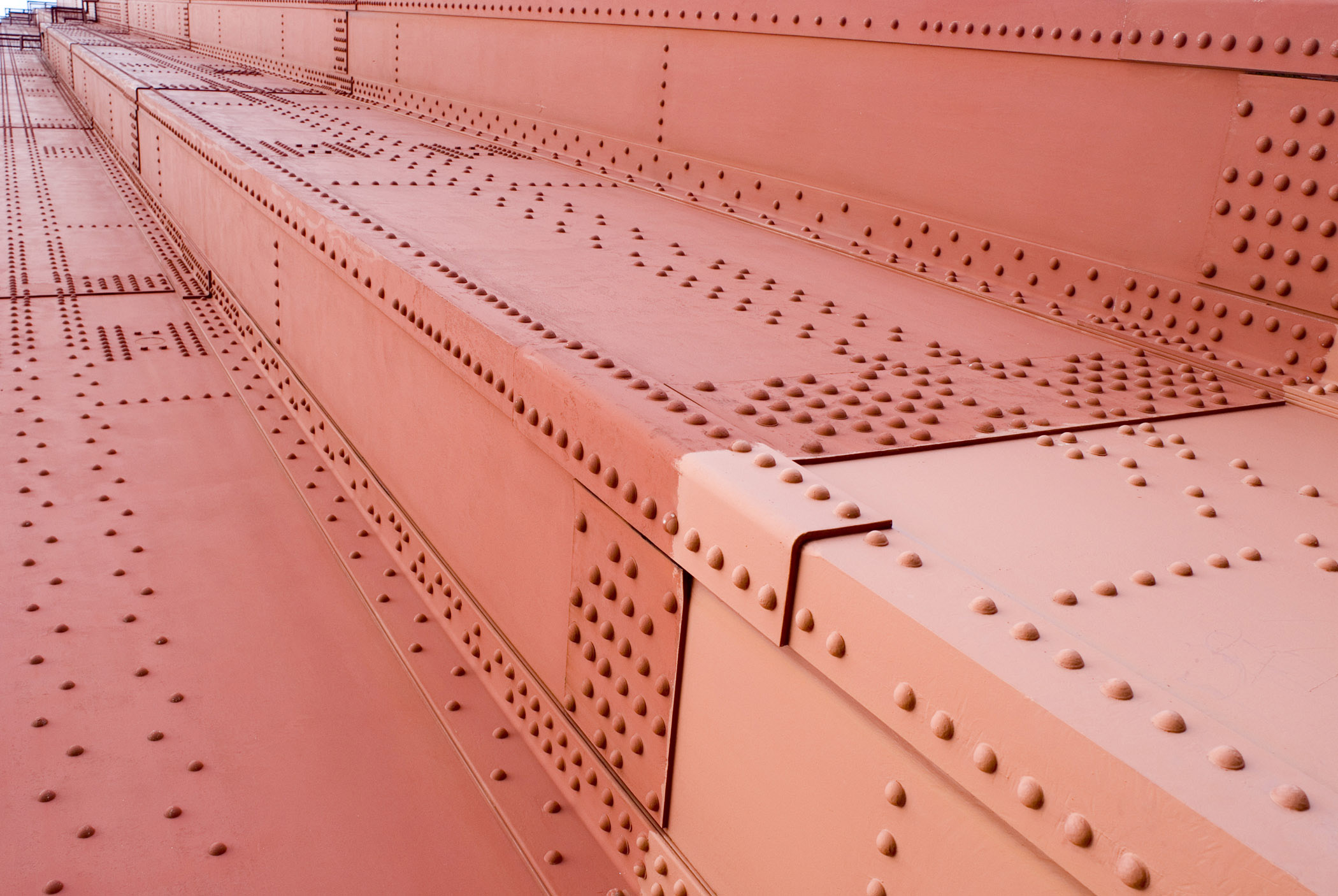 an image of Golden Gate Bridge details showing the structural engineering of rows of rivets on red painted metal sheeting