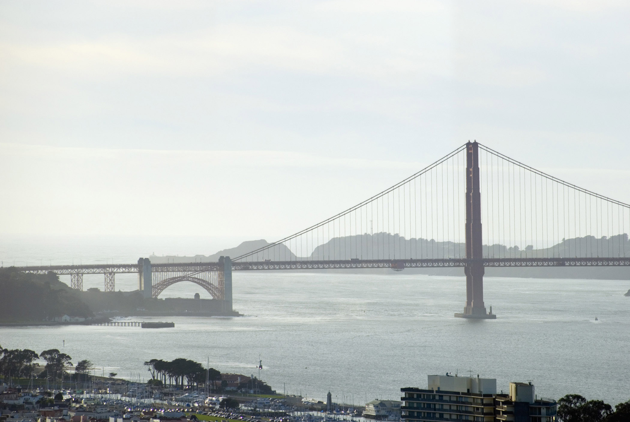 an image of Famous Long Golden Gate Bridge in San Francisco. Against a Very Light Blue White Sky Background.