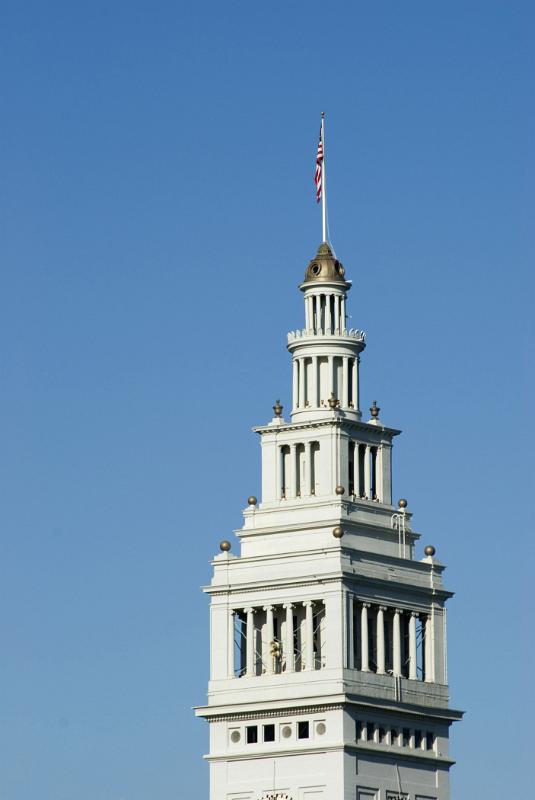 American Flag on Top of Architectural Ferry Building at Embarcadero, California. Captured on Lighter Blue Sky Background.