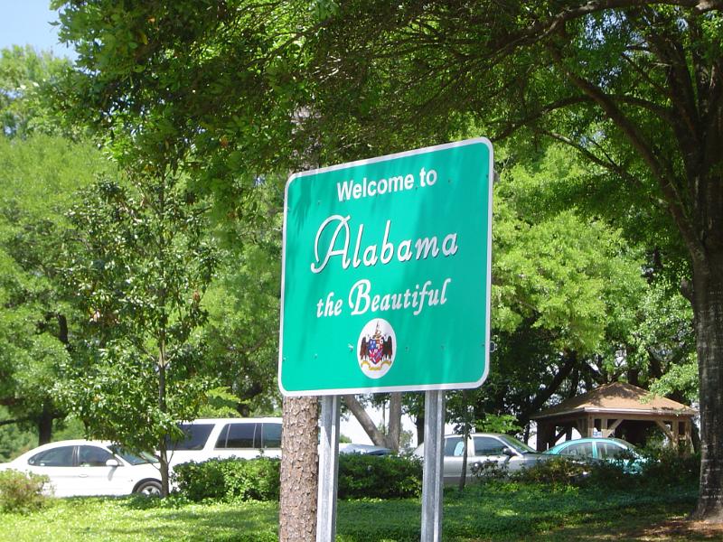 Alabama welcome road sign at the side of a leafy green street conceptual of a road trip vacation driving around the USA