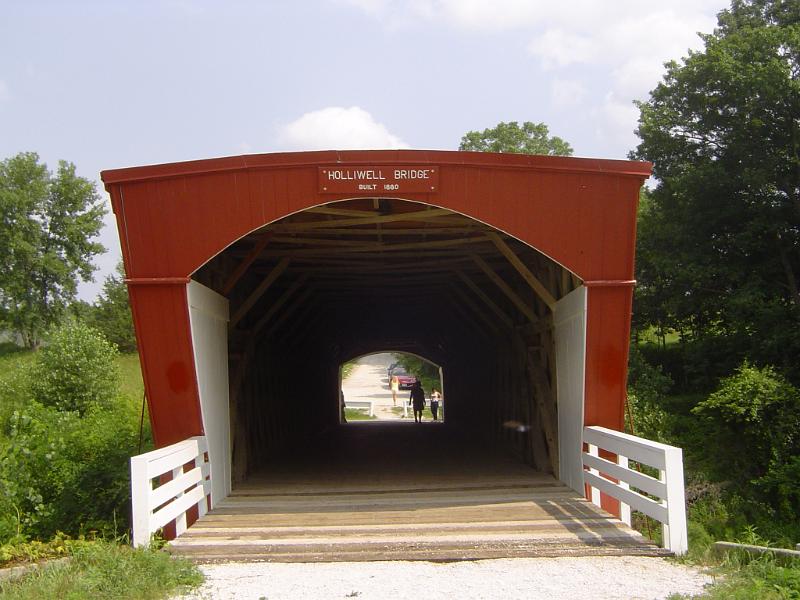 Entrance to an old historical covered wooden Madison County Bridge with neat white fences on either side of the opening and a view through to the other side