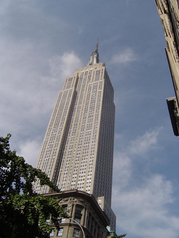 View from the street below looking up of the Empire State Building in New York against a cloudy blue sky