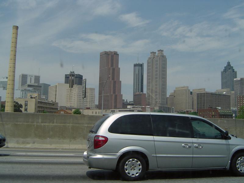 Freeway with passing vehicular traffic in front of a city skyline shrouded in smog