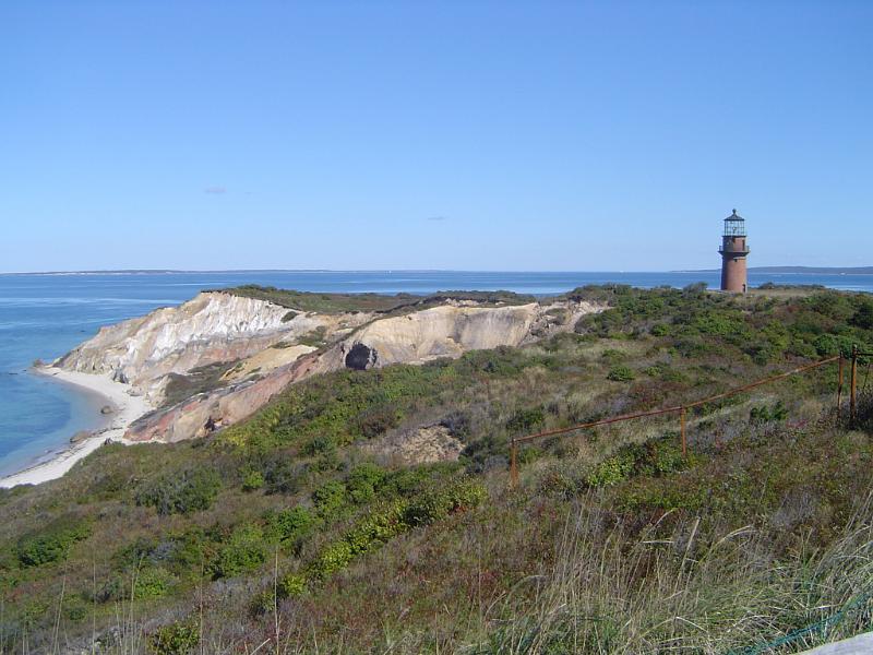 Lighthouse on Grassy Ocean Cliff Grassy Ocean Cliff with Lighthouse Afar in Extensive View. Isolated on Light Blue Sky Background.