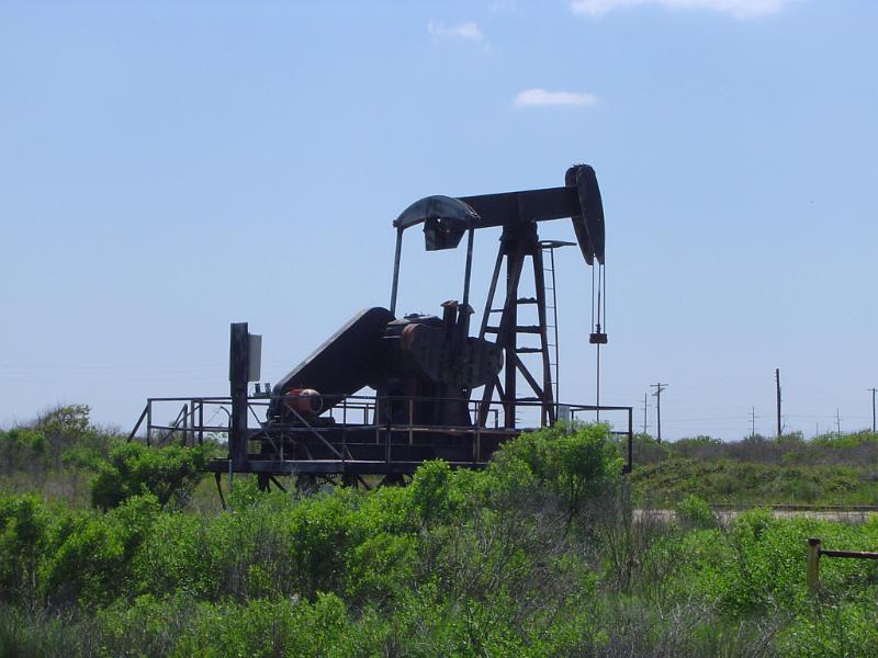 Iconic Nodding Donkey - Oil Well Pump Jack on Grassy Land. Captured on Light Blue Sky Background.