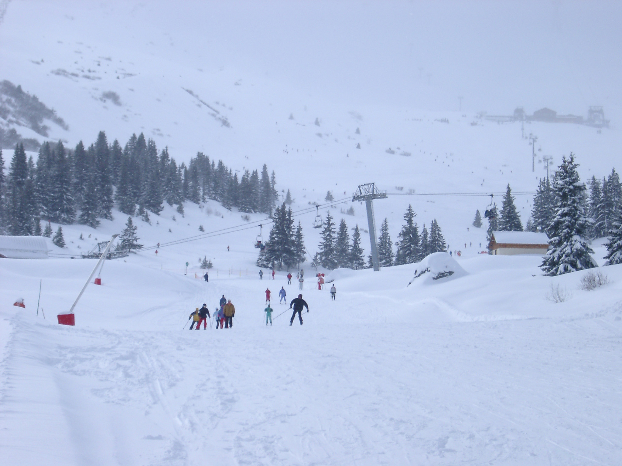 an image of Group of independent skiers on a broad fresh piste dotted with fir trees at a mountain resort with chair lift for access to the slopes, scenic winter landscape