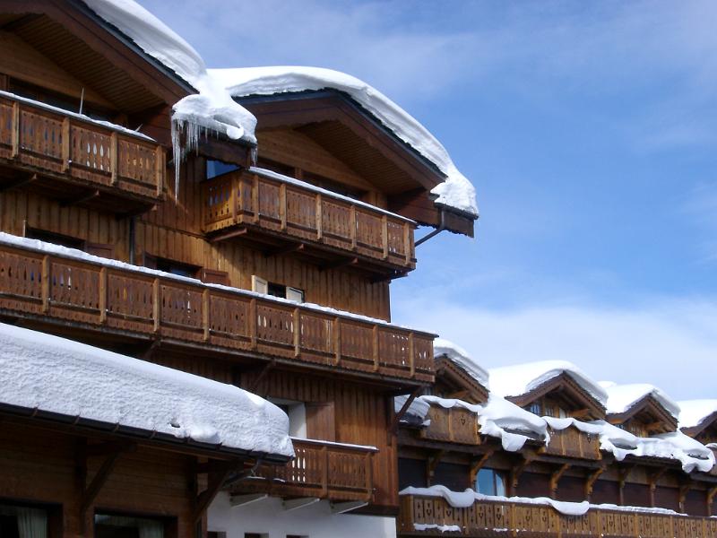 Snow on Vintage Wooden Alpine Lodge Building on Lighter Blue Sky Background During Winter.