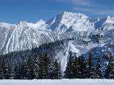 Steep rugged Alpine mountain peaks covered in winter snow towering above evergreen pine forests in a scenic landscape with a piste through the forest