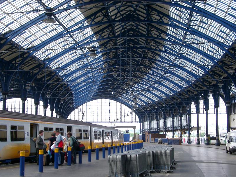 Interior of Brighton Station with its curved glassed roof and a train standing at the platform with visitors boarding