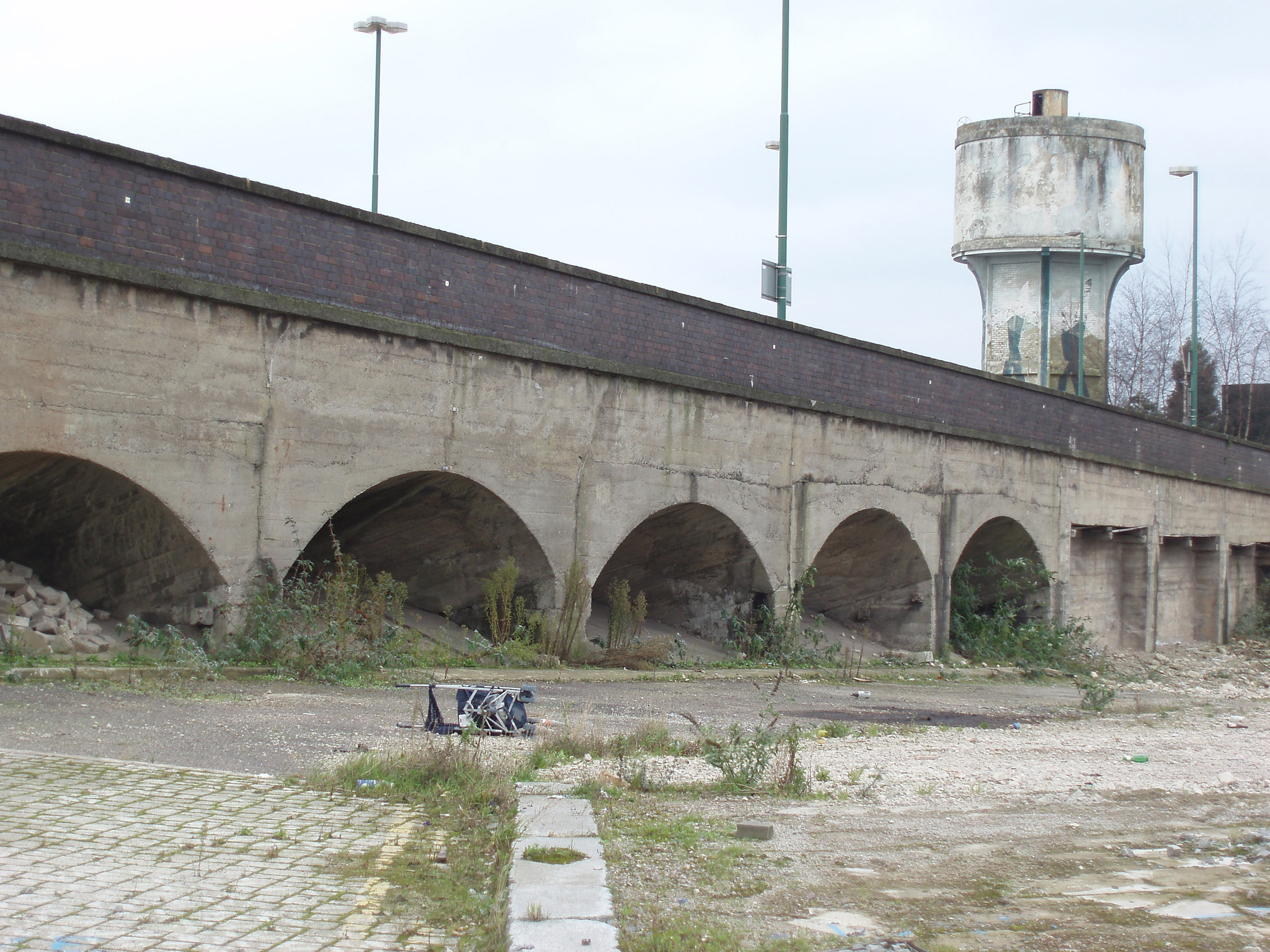 an image of Old grungy obsolete railway bridge with arches in urban wasteland with a concrete water tower