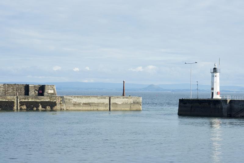 Breakwater and pier with lighthouse under partly cloudy sky in background at Anstruther, Scotland