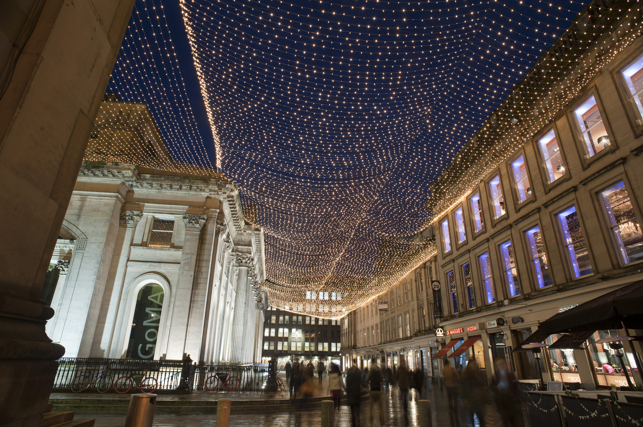 an image of Royal Exchange Square and GOMA, Glasgow at night with a low angle view of the exterior facade of the Gallery Of Modern Art and the display of illuminated Christmas lights above