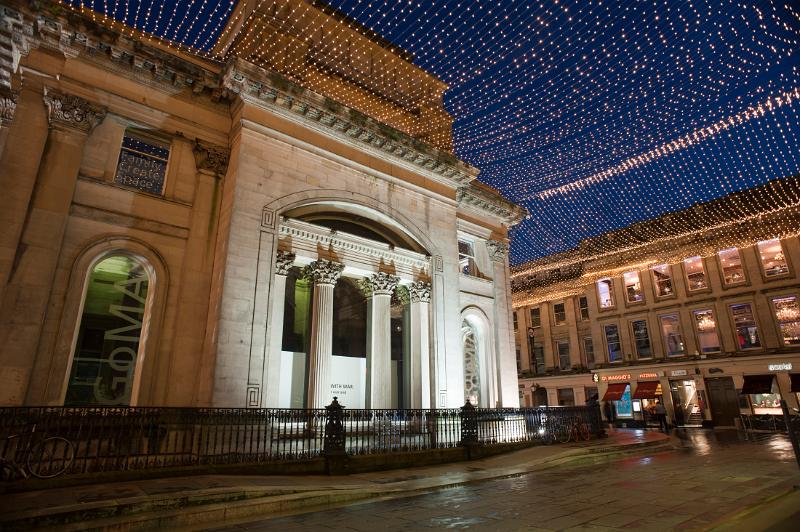 Royal Exchange Square and the GOMA, or Gallery of Modern Art, building in Glasgow illuminated at night with a display of overhead Christmas lights