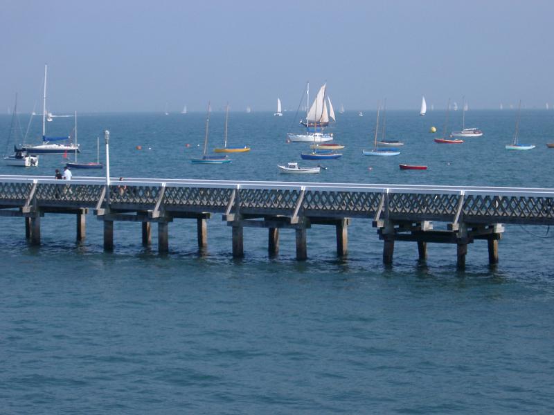 Jetty on the Isle of White in a calm ocean with small pleasure craft and sailboats moored offshore on the other side