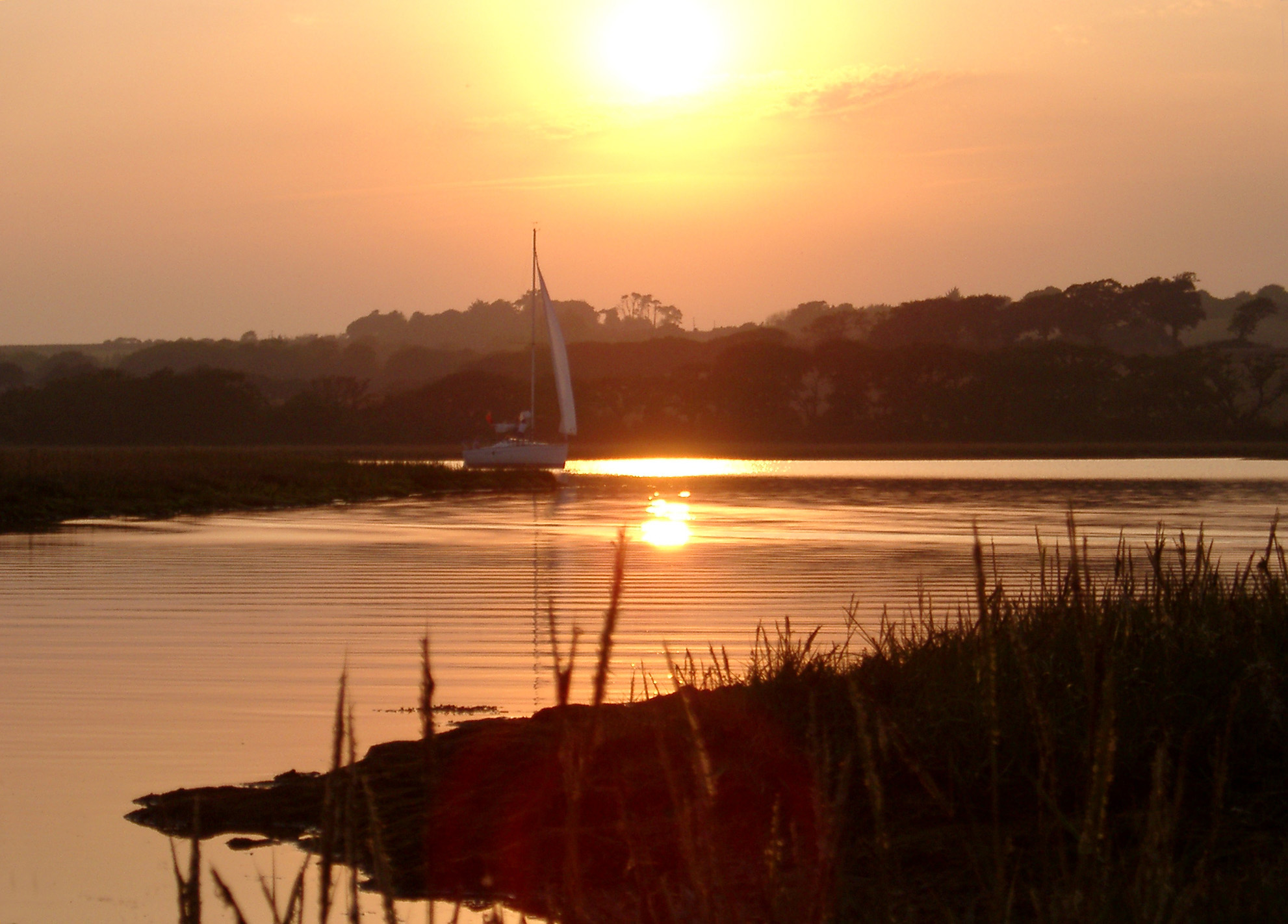 an image of River Yar, Isle of Wight, which starts at Freshwater Bay, on the south coast of the island and flows only a few miles north to Yarmouth viewed at sunset with the orange sun reflected in the calm water