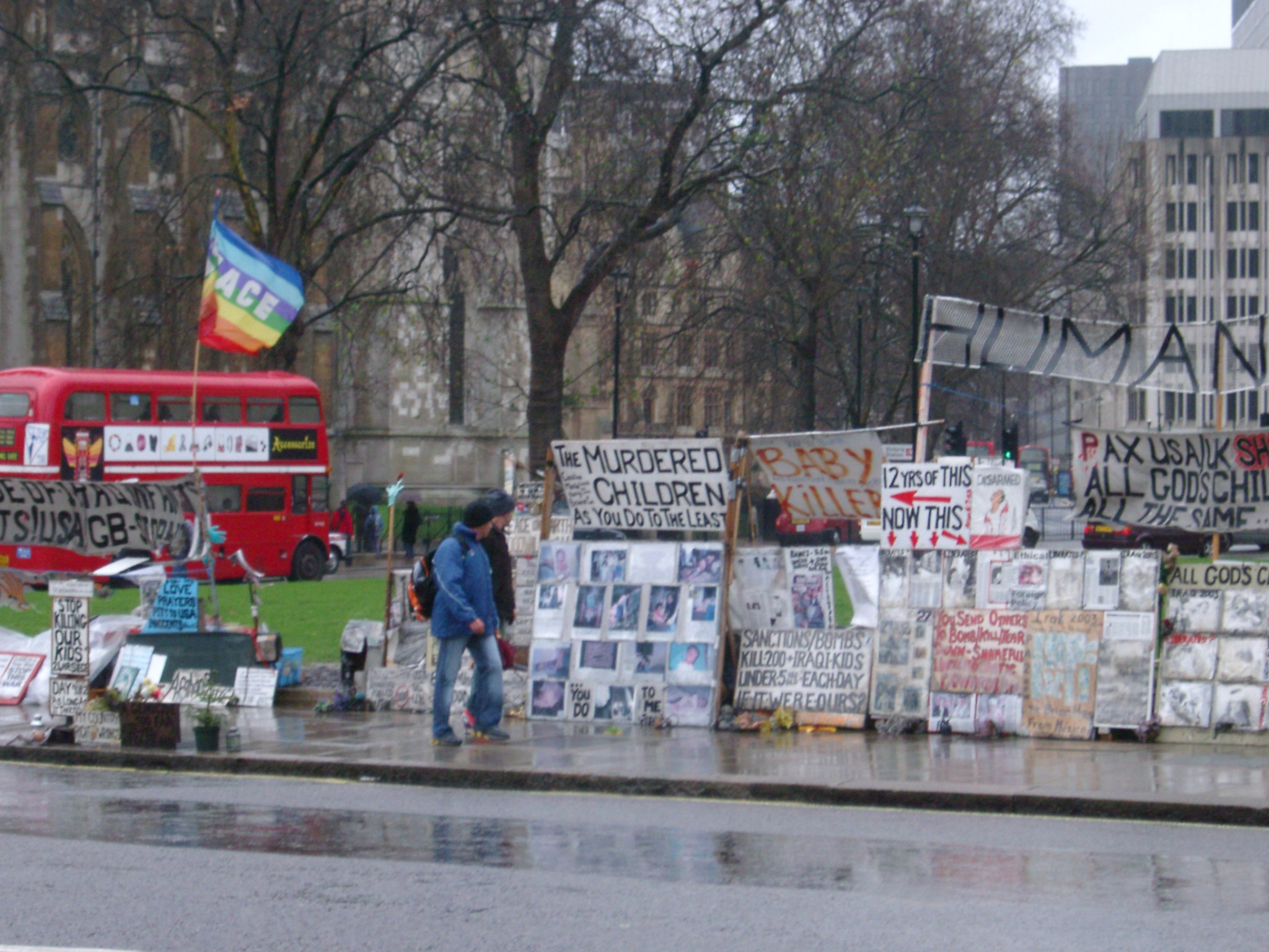 an image of Streetside demonstartion in London with a pedestrian walking past a display of placards and slogans on a wet rainy day
