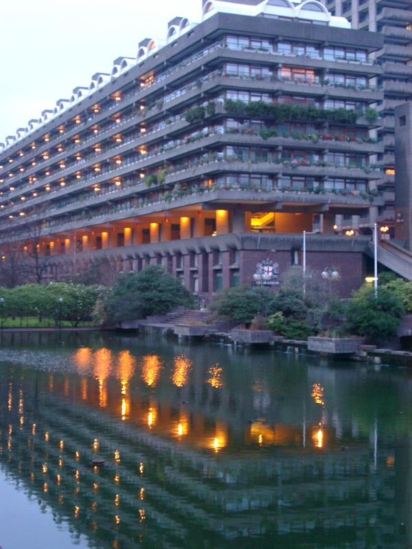 Barbican apartment block at dusk with the lights reflected in a pool below, London, England