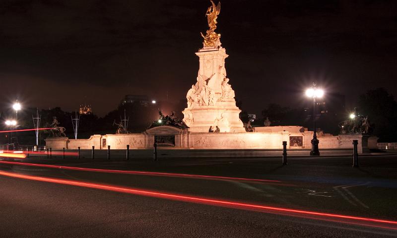 a night time view of the victoria memorial with gold statue of eros on top, located at the front of buckingham palace