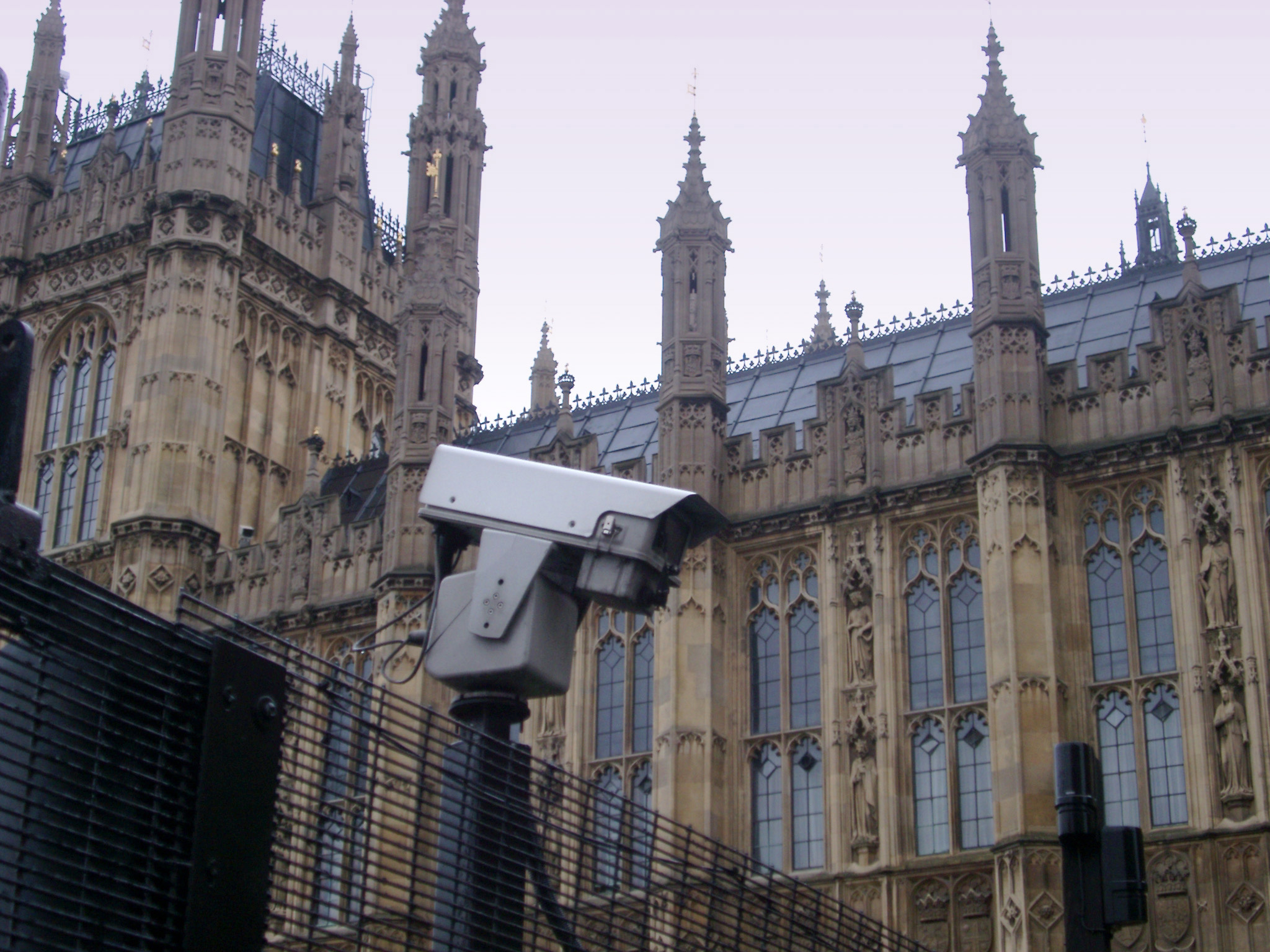 an image of Westminster, London, security showing a mounted surveiilance camera and closed circuit tv on a perimeter fence with the building behind