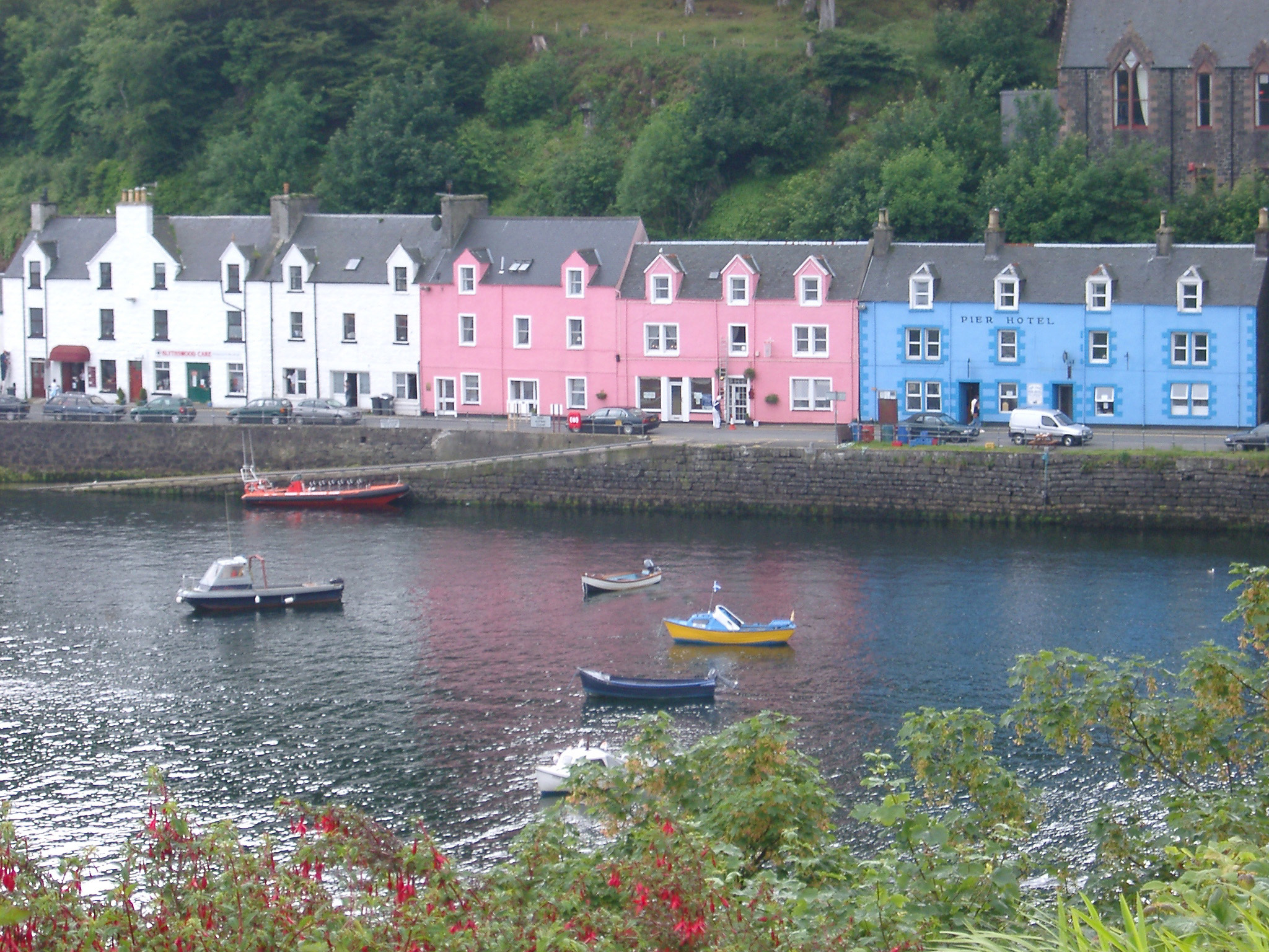an image of Colorful terraced houses and hotel on the waterfront overlooking fishing boats on the water in Portree, Isle of Skye