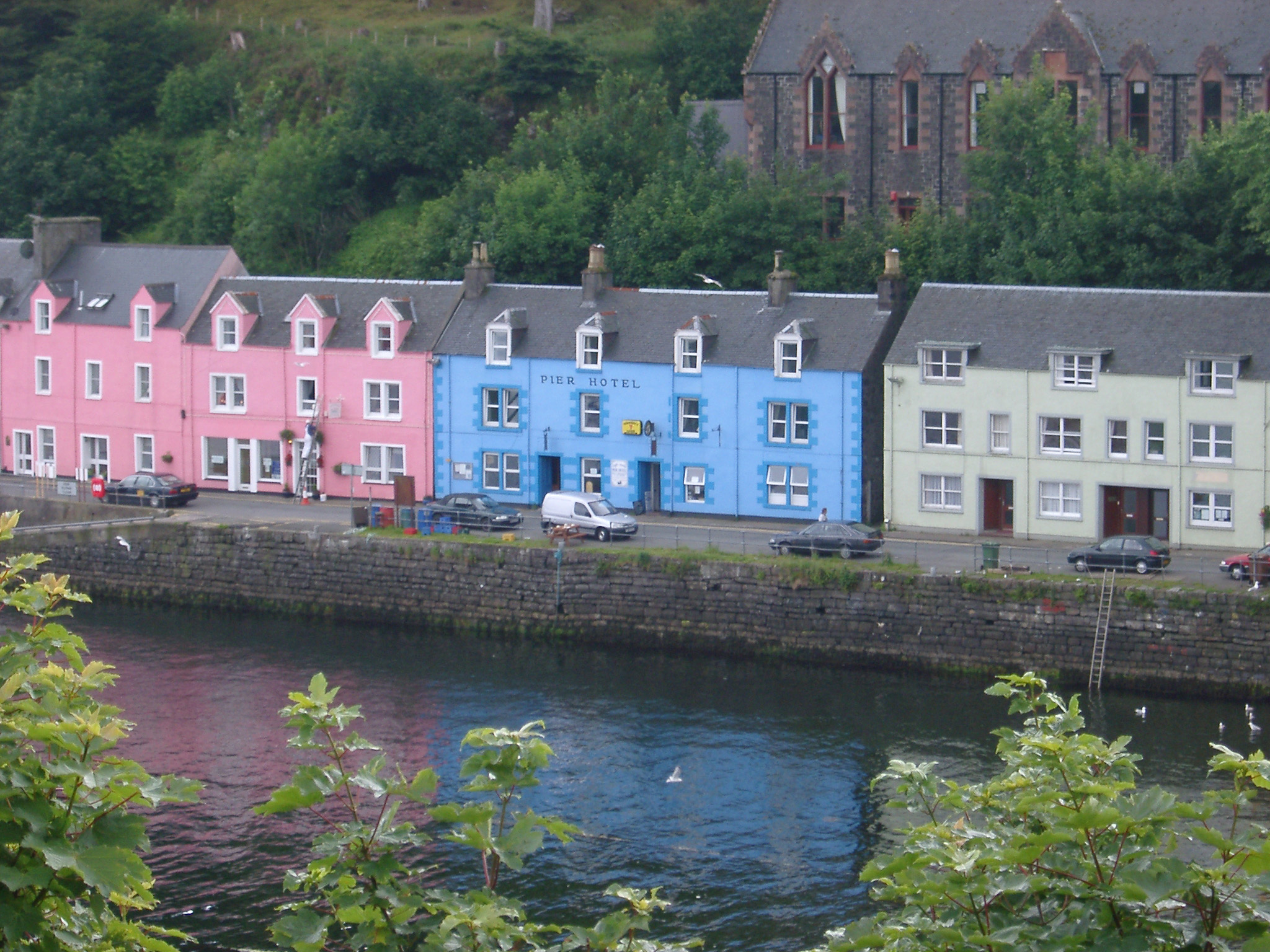 an image of Row of colorful fishermans houses on a terrace in Portree, Isle of Skye, painted pink, cyan and white