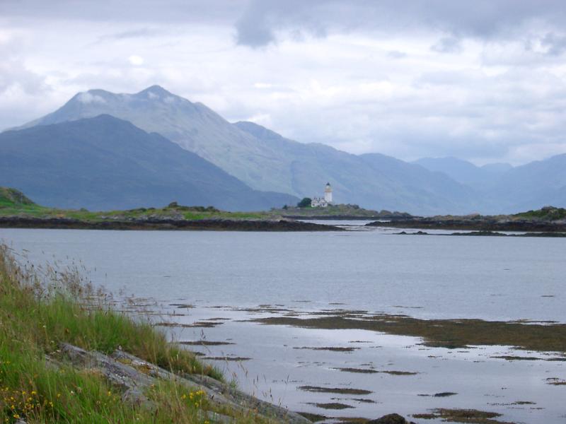 Scenic view of the Isle of Skye Scenic view across the water of the Isle of Skye and its lighthouse below mountain peaks on a sunny cloudy day