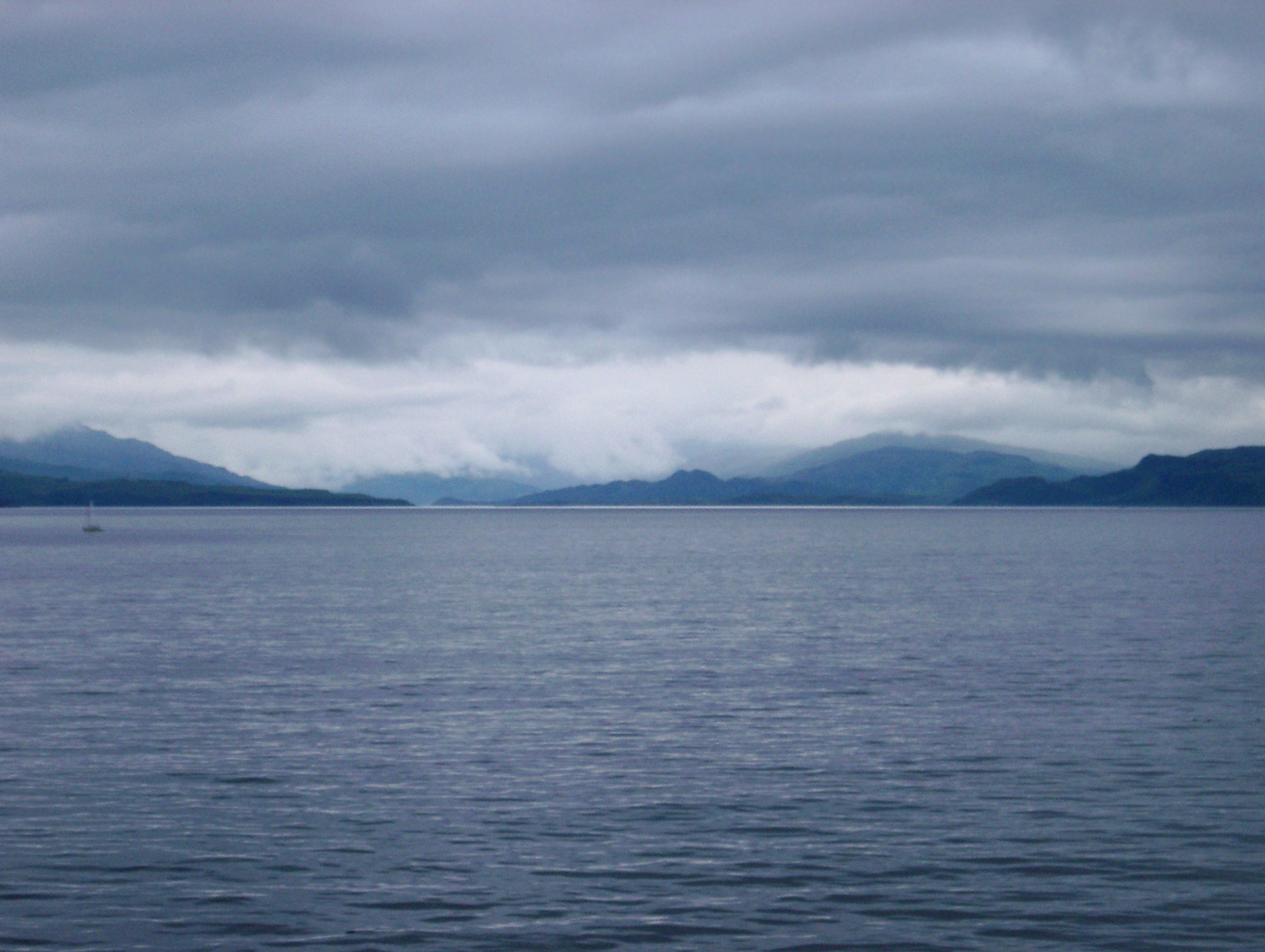 an image of View over a calm ocean on a stormy overcast day of Scottish lochs and distant mountains