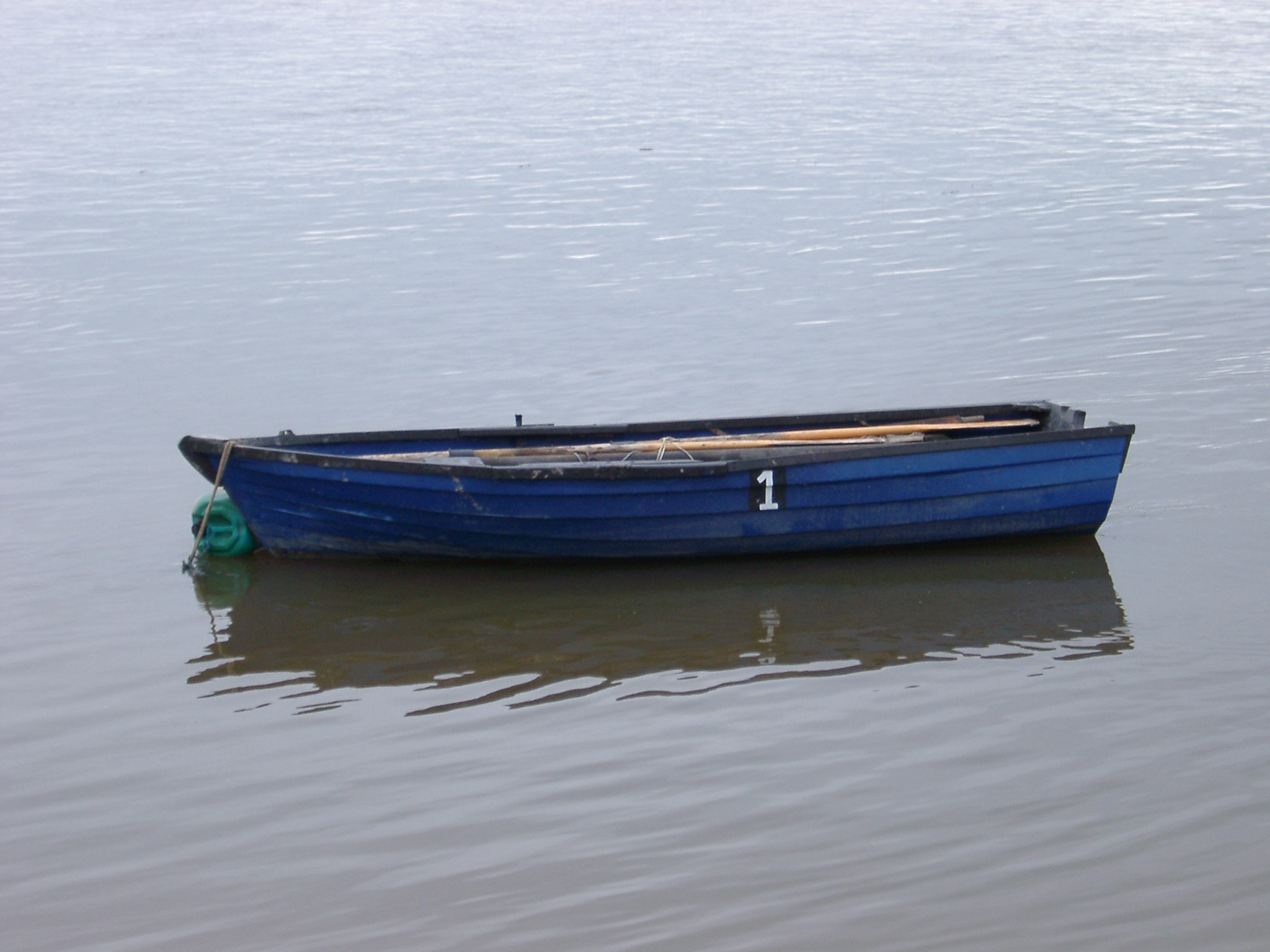 an image of Old wooden blue painted rowing boat moored in sheltered water with a reflection and copyspace