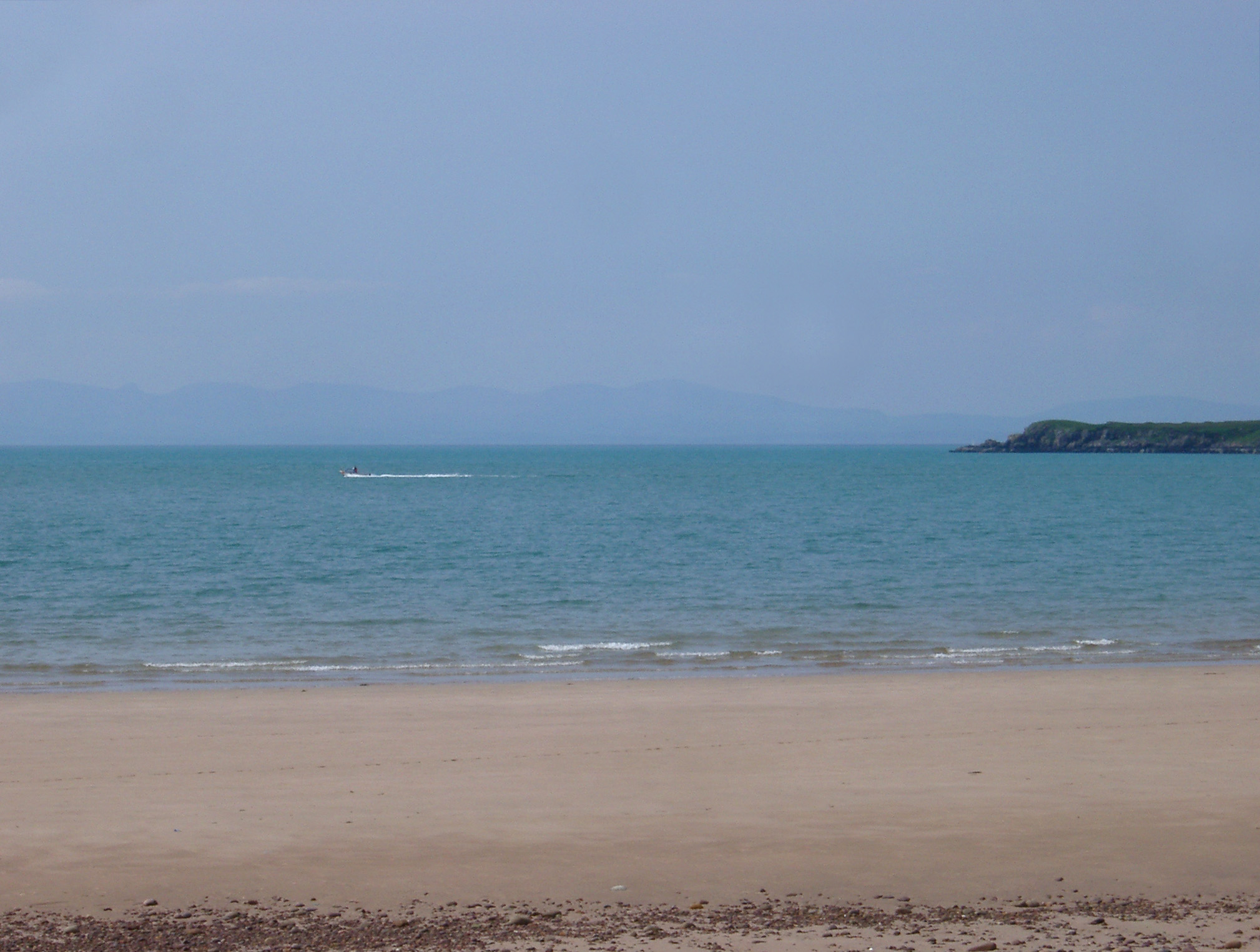 an image of Deserted sandy beach with golden sand and a calm blue sea on the Scottish coast with a headland in the distance