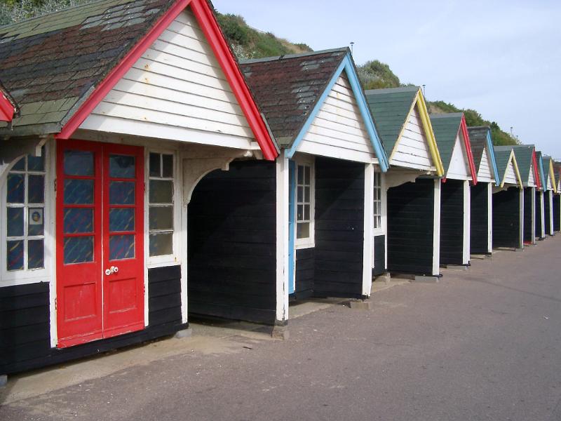 Wooden beach huts with border and doors painted in various colors, aligned along the seashore