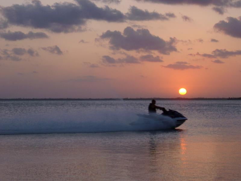 Jet ski at sunset throwing up a wake and spray of turbulent water as it speeds through the ocean silhouetted against a colorful cloudy sky