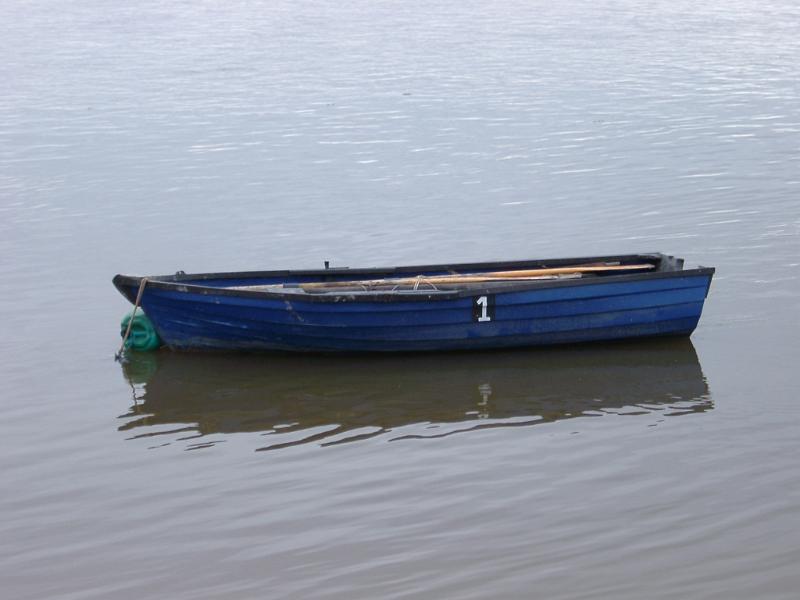Old wooden blue painted rowing boat moored in sheltered water with a reflection and copyspace