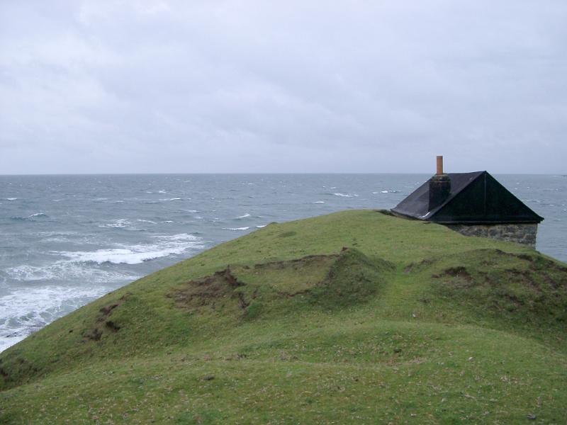 Seascape with a remote cottage Seascape with the roof of a remote cottage or shed just visible above the headland overlooking a stormy sea on an overcast day