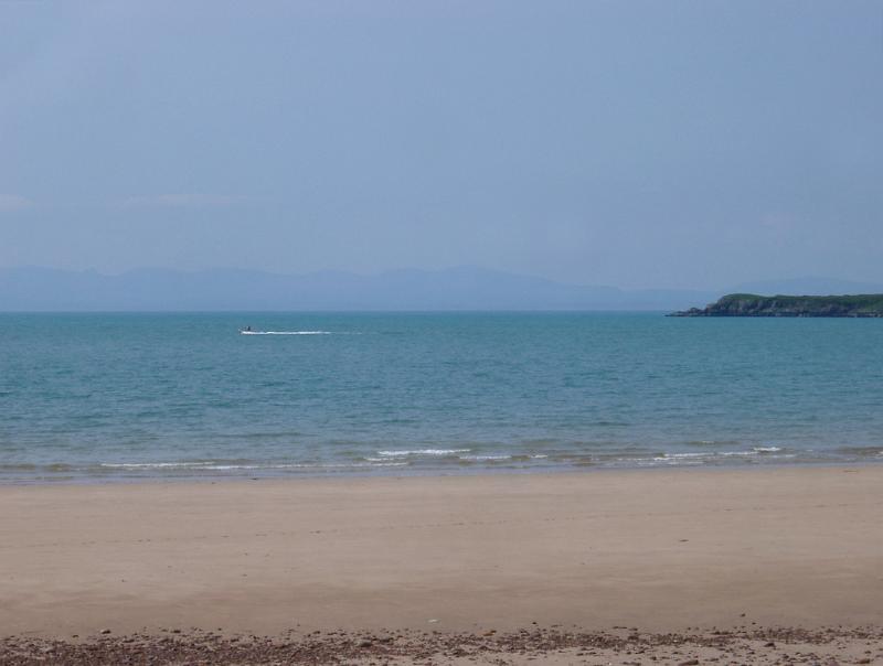 Sandy beach with a calm blue sea Deserted sandy beach with golden sand and a calm blue sea on the Scottish coast with a headland in the distance