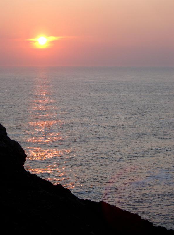 Fiery ocean sunset with the bright glowing sun surrounded by a halo casting a beam across the water to a silhouetted cliff on the Scottish coast