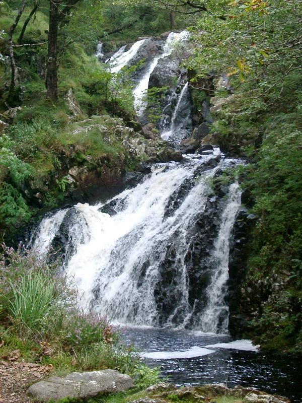 Double waterfall Double waterfall cascading down a mountain slope over rocks into a pool below through lush green woodland in a scenic landscape