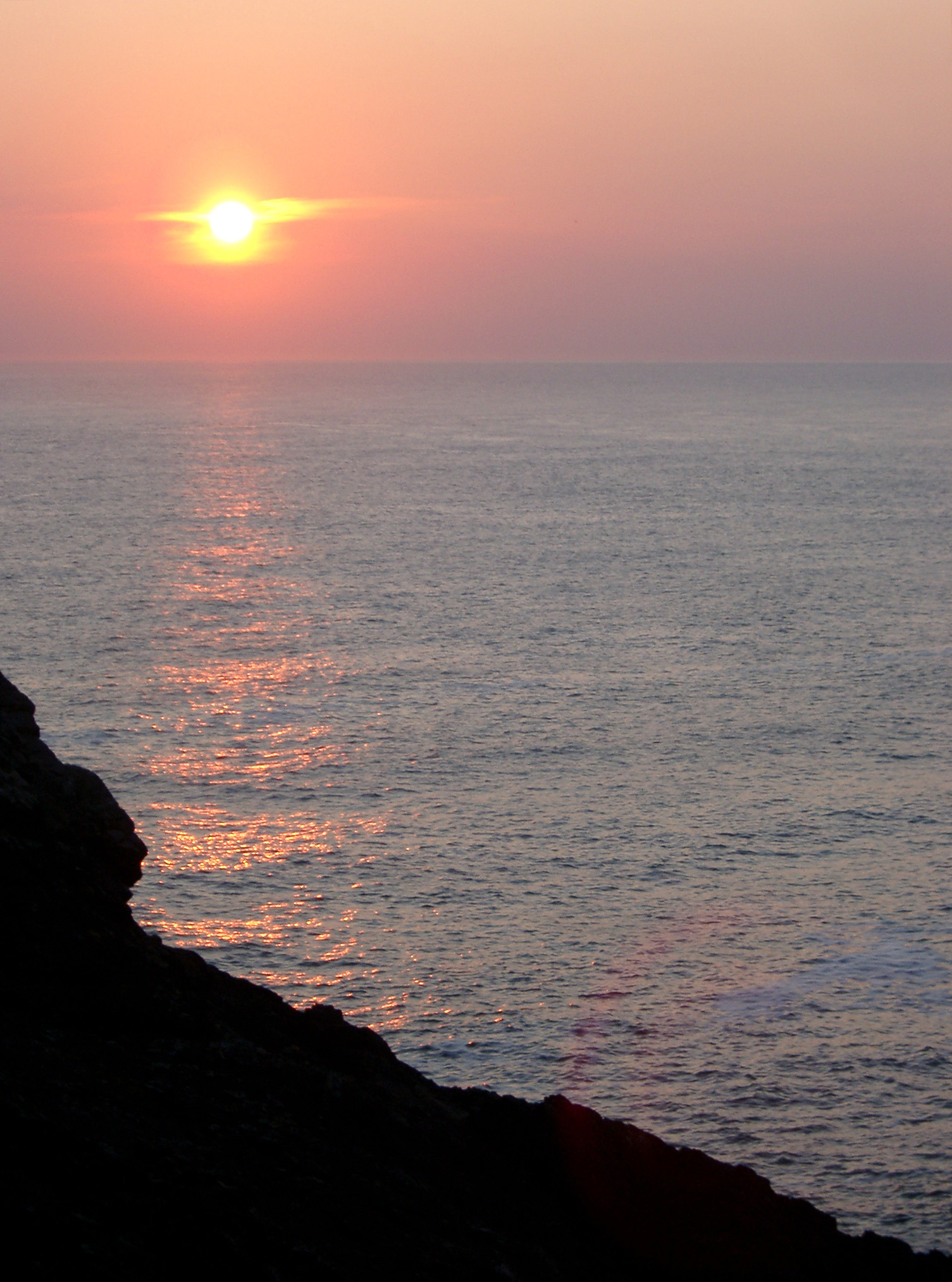 an image of Fiery ocean sunset with the bright glowing sun surrounded by a halo casting a beam across the water to a silhouetted cliff on the Scottish coast