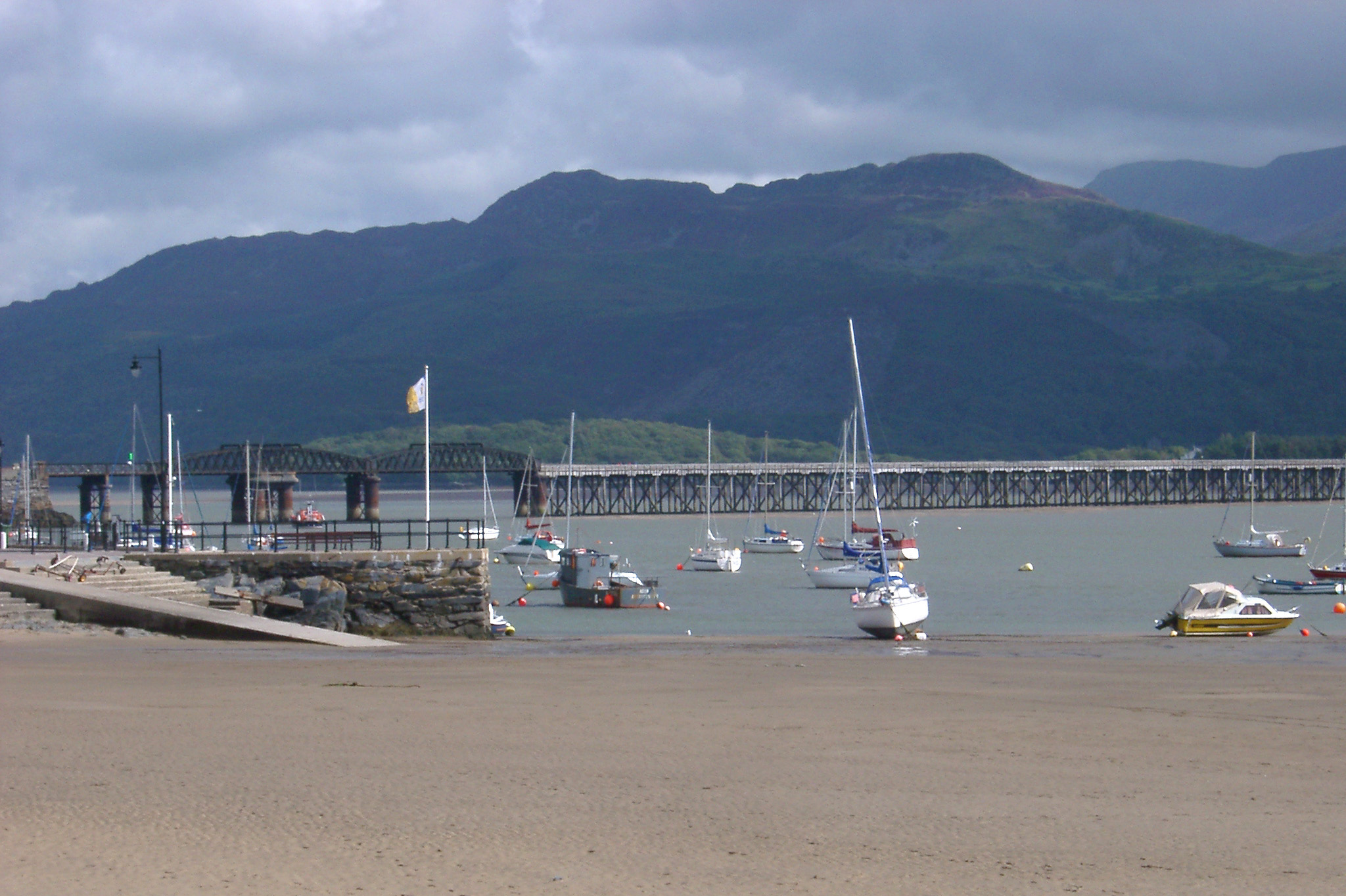 an image of Barmouth rail viaduct with small fishing and pleasure boats moored in the sheltered harbour in the foreground