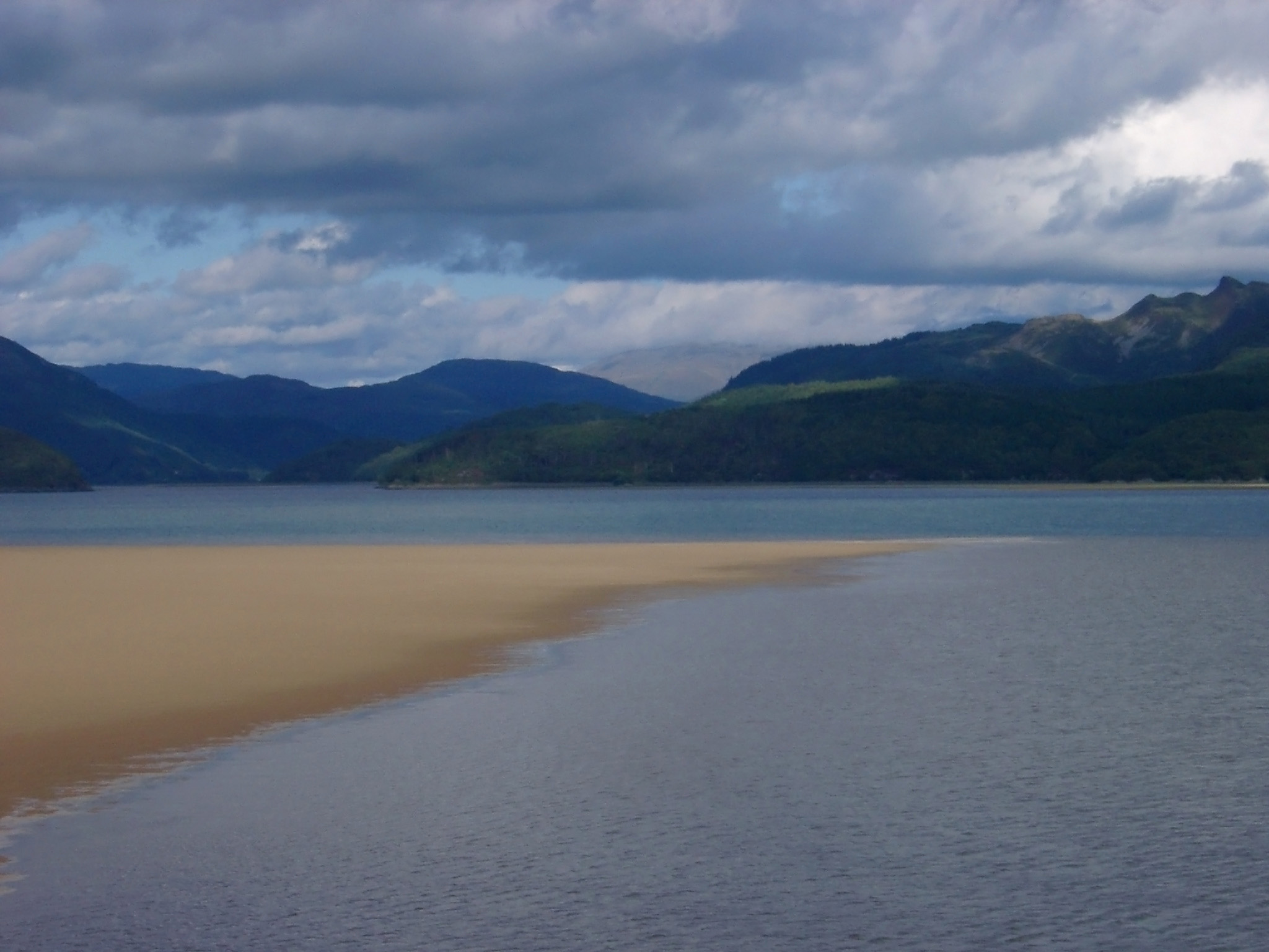 an image of Tranquil Waterside with Brown Sand, Captured with Mountains View