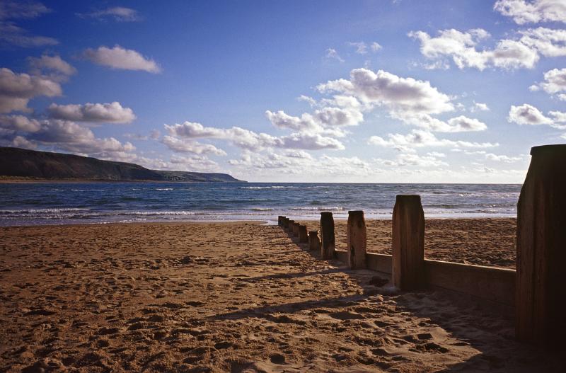 Row of stone groynes on Barmouth beach to protect the coastline from erosion by the tides and waves on a sunny summer day with fluffy white clouds