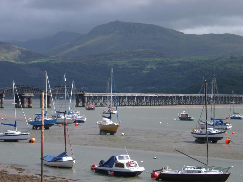 Fishing boats moored in the harbour at Barmouth with the steel railway viaduct crossing the water behind them against a mountain backdrop