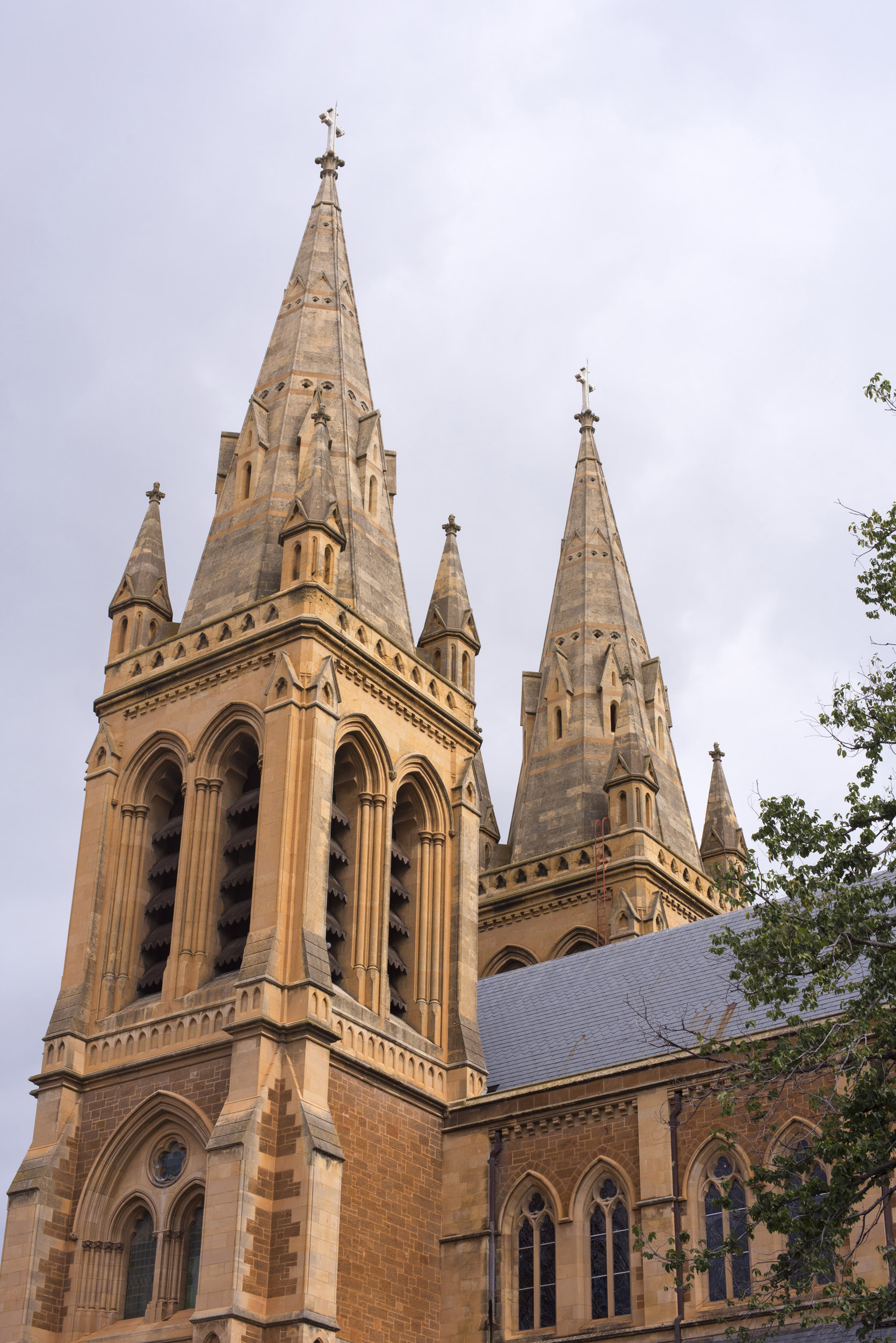 an image of Ornate stone spires of Adelaide Cathedral, Australia against a cloudy grey sky viewed from below