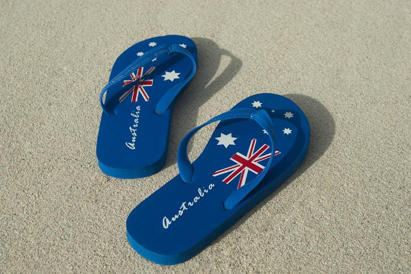 A pair of blue Australia day thongs with national flag design on a sandy beach.