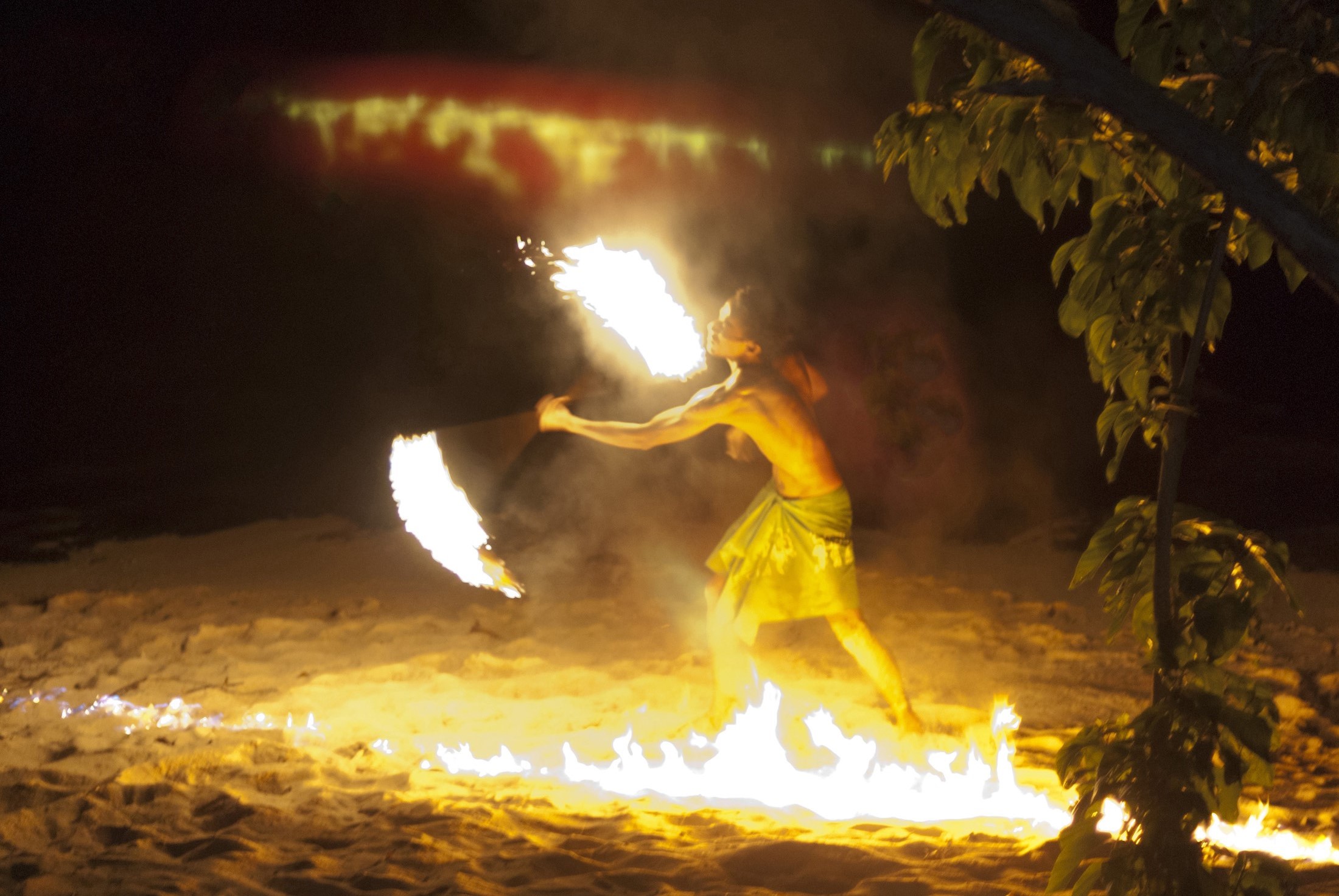 an image of Fijian fire dancer performing on a beach amidst tongues of orange flames
